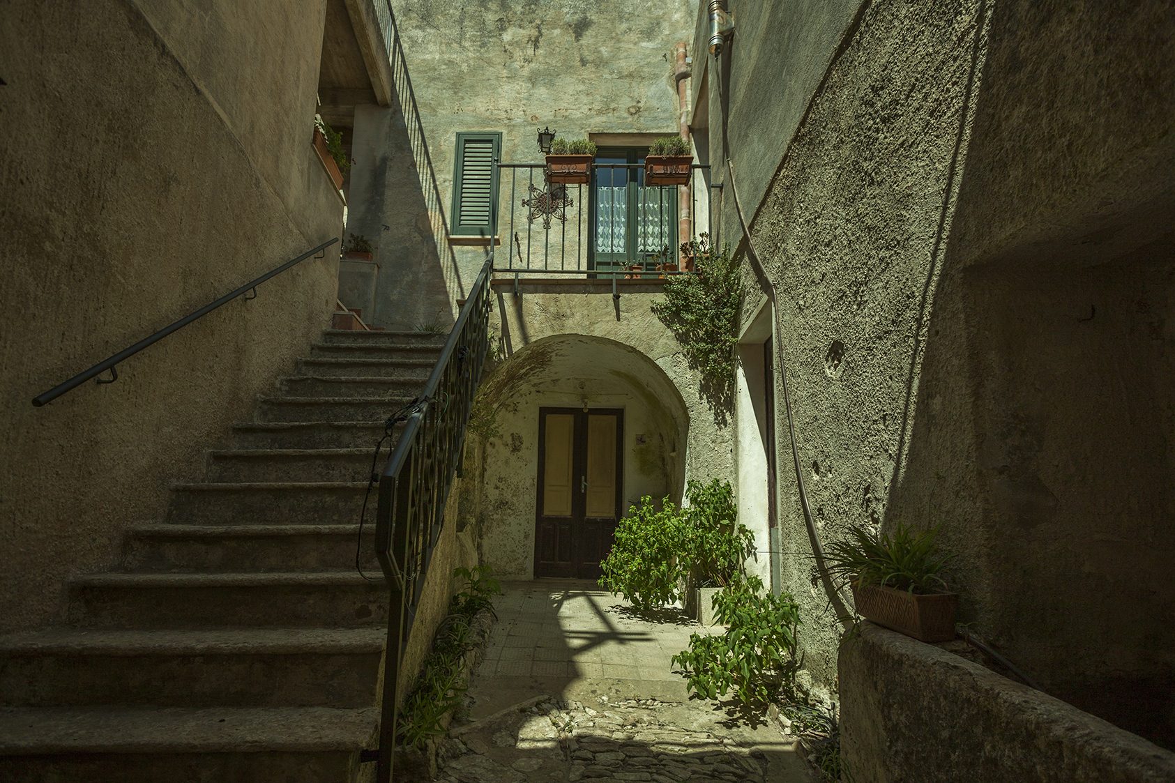 A narrow medieval lane in Erice, paved in grey limestone, opening toward a distant view of the Sicilian coast.